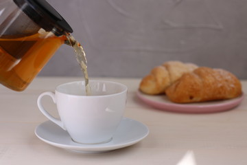 tea pouring into cup and croissant dessert on light wooden background