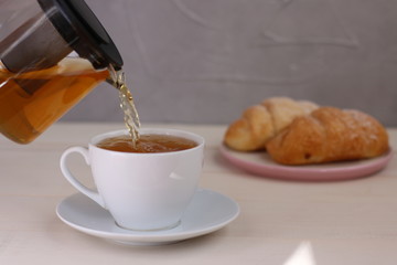 tea pouring in cup on light background. teapot and breakfast concept