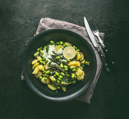 Bowl with potatoes salad with roasted green asparagus, edamame soybeans, lime and green peas on dark rustic kitchen table background, top view. Copy space. Healthy vegetarian food .