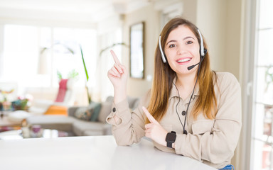 Beautiful young operator woman wearing headset at the office smiling and looking at the camera pointing with two hands and fingers to the side.