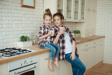 Mom and daughter have fun in the kitchen, chatting, drinking tea and eating croissants