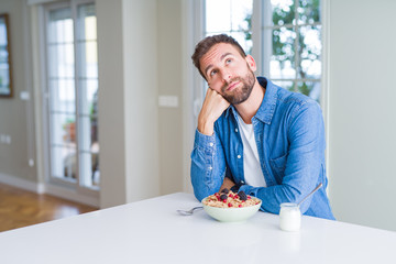 Handsome man eating cereals for breakfast at home with hand on chin thinking about question, pensive expression. Smiling with thoughtful face. Doubt concept.
