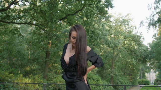 East European girl wearing a black dress and high heels, sensually dancing in a park. Slow motion footage with a majestic castle in the background.