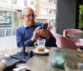 Fototapeta na wymiar Handsome middle age senior man drinking coffee at restaurante, smiling happy enjoying and relaxing retirement using smartphone