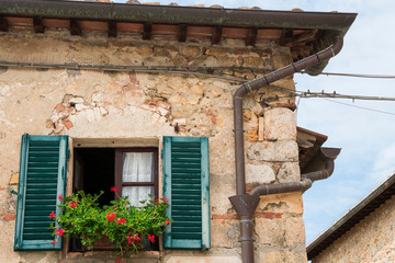 Fototapeta na wymiar Window with shutters, geranium and electrical wire in Monteriggioni, Italy