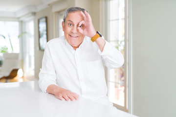 Fototapeta premium Handsome senior man at home doing ok gesture with hand smiling, eye looking through fingers with happy face.