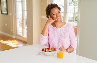 Young african american woman having healthy breakfast in the morning at home smiling doing phone gesture with hand and fingers like talking on the telephone. Communicating concepts.