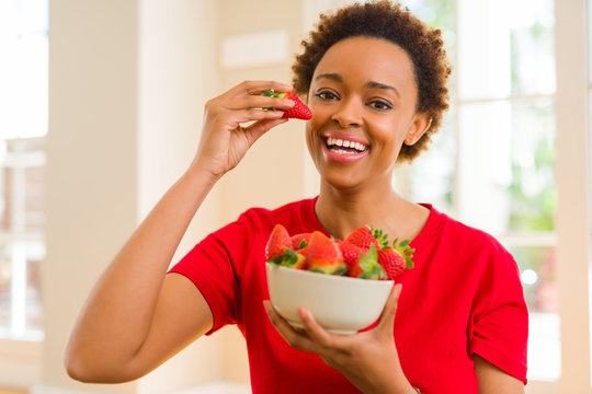 Beautiful young african woman with afro hair eating fresh strawberries