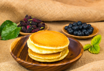 Pile of pancake in wooden bowl with mulberry and blueberry in wooden plate