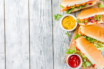 Homemade hot dogs with fresh greens, sausages and sauces, white wooden background copy space top view