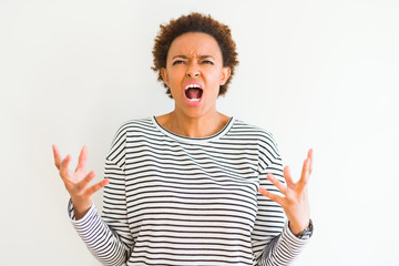 Young beautiful african american woman wearing stripes sweater over white background crazy and mad shouting and yelling with aggressive expression and arms raised. Frustration concept.