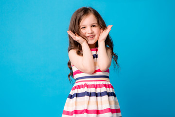 baby girl brunette in colorful dress smiling, isolate on blue background, children's emotions,Close-up portrait of dark-haired little girl  smiling on isolated background 