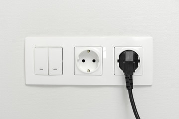 Electrical sockets on the wall with black connection plug and white switch.