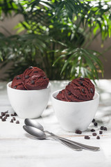 Chocolate ice cream bowls and chocolate chips on the white wooden table.