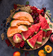 Fresh summer fruits and berries on a round cutting board, watermelon, cantaloupe, cherries, current, square image