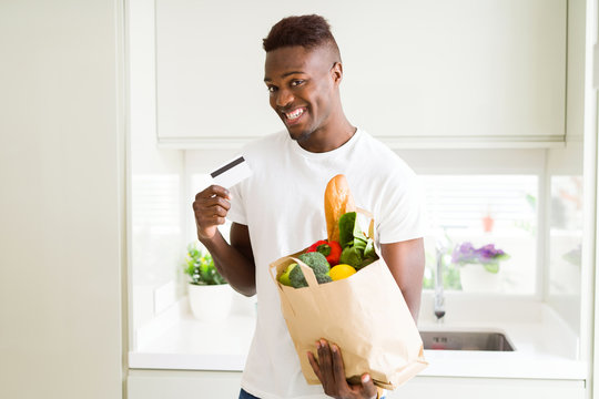African american man holding paper bag full of groceries and holding credit card as payment
