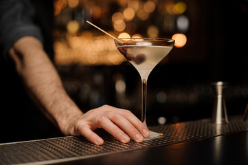 Close-up of alcohol cocktail with olives under bartender's hand