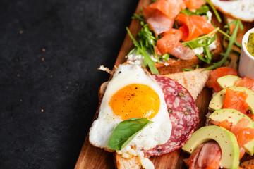 Appetizers table with healthy snacks. Brushetta or sandwich set on the board over black concrete background.