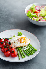 Blanched asparagus, fried egg, tomatoes and sald on the bowl. Breakfast concept
