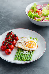 Blanched asparagus, fried egg, tomatoes and sald on the bowl. Breakfast concept