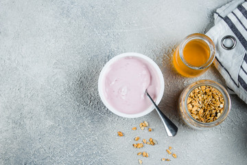 Healthy Breakfast Concept. Strawberry or raspberry yogurt, granola and honey on light concrete table background. View from above with copy space. Flat lay