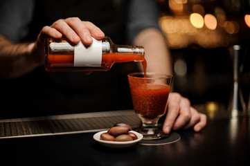 Bartender makes bloody mary cocktail with red olives