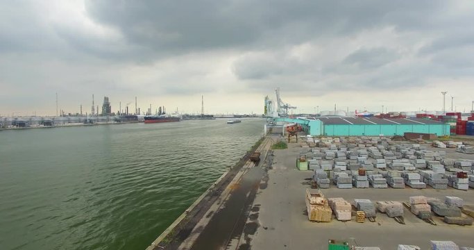 Following a ship with a drone on the Scheldt river surrounded by cargo ships, machinery, granite blocks, far view from the nuclear station in Doel.