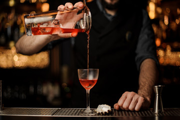 Bartender pours an alcohol cocktail using jar with sieve