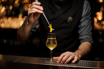 Bartedner adds lemon rind with forceps in cocktail