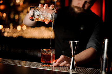 Bartender makes alcohol cocktail using glass with strainer