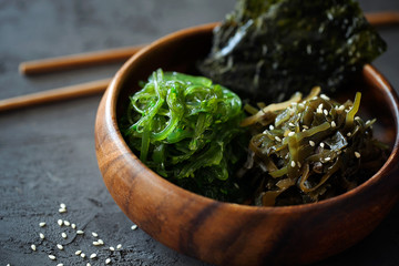 Traditional Japanese Snack - Chuka Wakame seaweed salad and crispy roasted nori sheets in wooden bowl on dark background close-up.Healthy seafood high in vitamins.Horizontal orientation