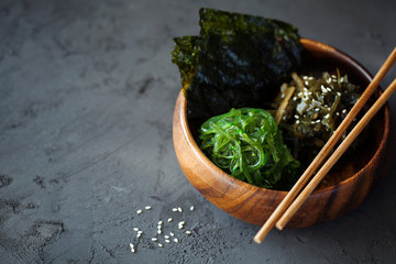 Traditional Japanese Snack - Chuka Wakame seaweed salad and crispy roasted nori sheets in wooden bowl on dark background top view with copy space for text.Healthy seafood high in vitamins - obrazy, fototapety, plakaty