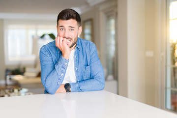 Young handsome man at home looking stressed and nervous with hands on mouth biting nails. Anxiety problem.