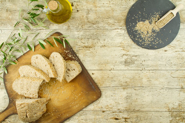 Close-up of a sliced loaf of homemade bread with sesame seeds, ampoule of extra virgin olive oil and an olive branch on wooden table background shot from above