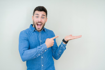 Young handsome man over isolated background amazed and smiling to the camera while presenting with hand and pointing with finger.