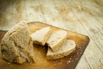 Close-up of a sliced  loaf of homemade bread with sesame seeds in selective focus on wooden table background