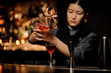 Bartender pouring cocktail using glass with a strainer