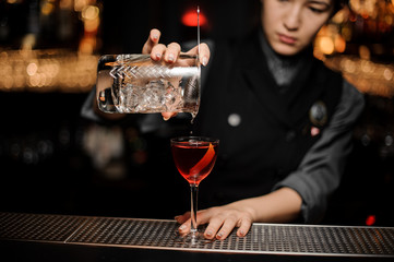 Bartender making alcohol cocktail using glass with strainer