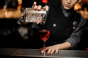 Bartender makes cocktail using glass with strainer
