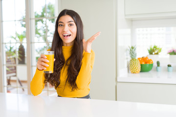 Young woman drinking a glass of fresh orange juice very happy and excited, winner expression celebrating victory screaming with big smile and raised hands