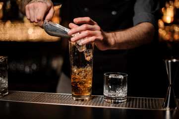 Male bartender adds ice in glass with ice scoop
