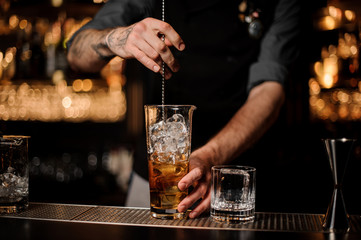 Male bartender stirring alcohol cocktail with bar spoon