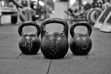 Fototapeta na wymiar Тhree black iron kettlebells with markings 24 and 16 kg standing close to each other. Gym and fitness equipment. Workout tools