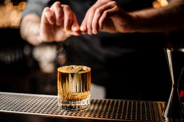 Bartender squeezes the lemon rind in alcohol cocktail