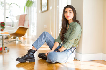 Young beautiful woman sitting on the floor at home with serious expression on face. Simple and natural looking at the camera.