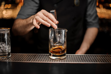Bartender adds ice in glass with ice tongs