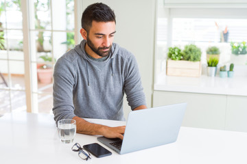 Fototapeta premium Handsome hispanic man working using computer laptop with a confident expression on smart face thinking serious