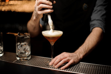 Fototapeta na wymiar Bartender pours an alcohol cocktail adding foam