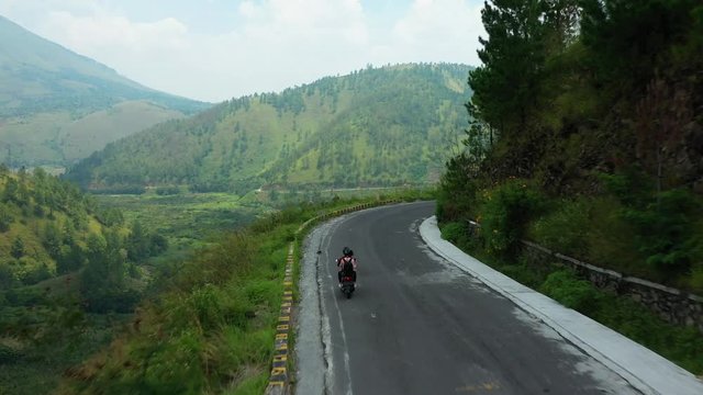 Aerial drone tracker footage of two scooter riders on a ride through cliffs overlooking Lake Toba in North Sumatra, Indonesia.