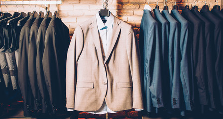 Men formal wear. Classy outfit. Modern clothing store. Business suit jackets and vests hanging,...
